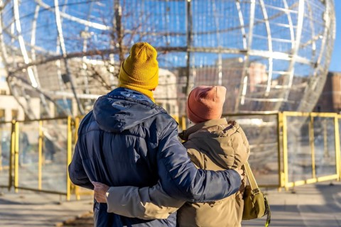 Elderly couple embracing while admiring large christmas ball decorations in a winter cityscape