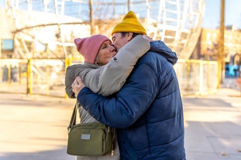 Elderly couple sharing a tender kiss and hug in a festive winter cityscape, celebrating love and