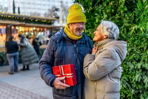 Loving senior couple exchanging christmas gifts at a festive outdoor market, enjoying the holiday