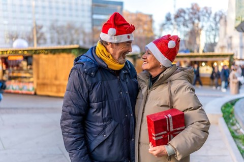 Loving senior couple wearing santa hats exchanging christmas gifts at a christmas market in the