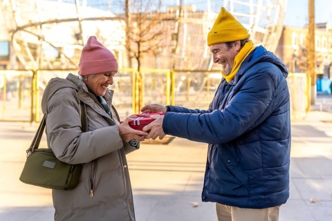 Happy senior man giving christmas present to smiling woman in amusement park during winter holidays