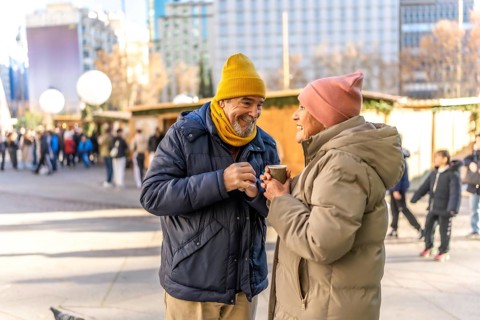 Smiling senior couple holding hot beverages and enjoying each other's company at a bustling