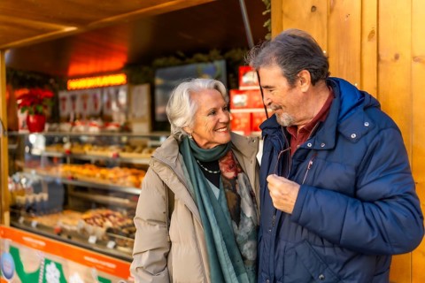 Elderly couple smiling and looking at each other in front of a food stall at a christmas market