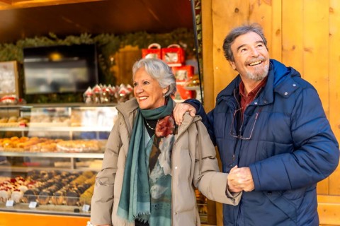Smiling senior couple holding hands and visiting a traditional christmas market, enjoying winter