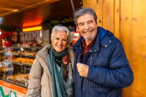 Cheerful retired couple enjoying christmas market during winter holidays, buying presents and