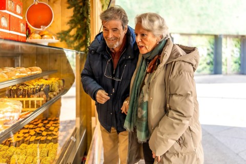 Happy retired couple selecting delicious sweets and cakes at a charming wooden stall in a festive