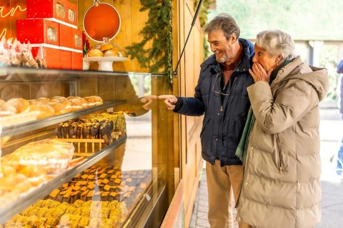 Joyful elderly couple pointing at delicious pastries in a bakery display window at an outdoor