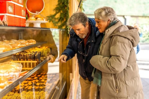 Elderly couple pointing and choosing delicious pastries from a market stall display during the