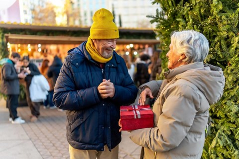 Elderly man and woman exchanging gifts at a christmas market in the city during winter holidays