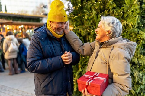Loving senior couple exchanging christmas gifts at a traditional christmas market, enjoying festive