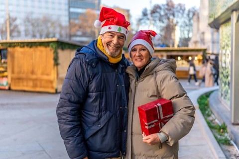 Smiling senior couple wearing santa hats holding christmas present at a christmas market in the