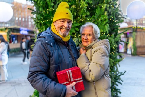 Smiling senior couple holding christmas gift, enjoying christmas market in the city during winter