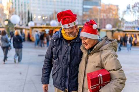 Smiling senior couple wearing santa hats holding hands and enjoying christmas market in the city