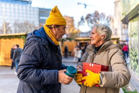 Happy senior couple exchanging christmas gifts and enjoying a warm beverage at a bustling outdoor