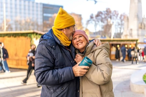 Affectionate senior couple enjoys warm drinks at a christmas market in a winter city setting