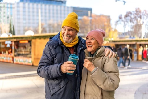 Smiling senior couple enjoying hot drinks at an outdoor christmas market, embracing the festive