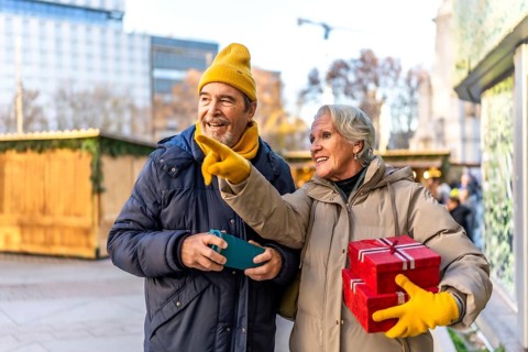 Cheerful senior couple holding christmas gifts and pointing at something interesting at the
