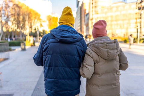 Elderly couple wearing winter clothes and colorful beanies enjoying a walk in a city park during