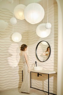 A woman dressed in a sparkling gown admires her reflection in a round mirror. Soft, textured walls