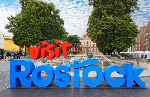 Vist Rostock logo, behind it fountain of joie de vivre, behind it university, university square,