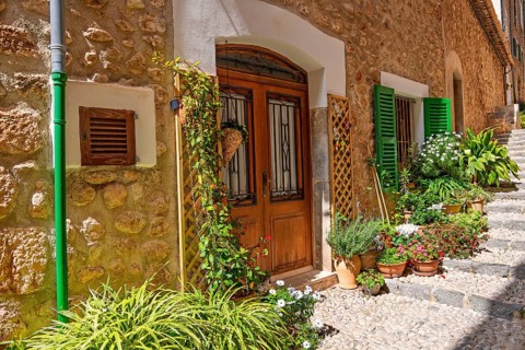 Apartment door with flowers and green plants outside on a stair in a cobblestone alley a sunny