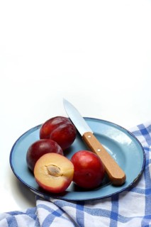 Red plums on plate with kitchen knife, Prunus domestica