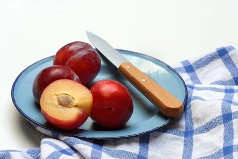 Red plums on plate with kitchen knife, Prunus domestica