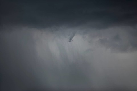 Aircraft breaks through cloud cover and drags a visible wake of vortices behind it