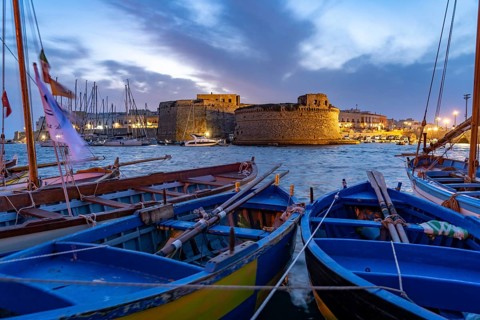 Typical fishing boats and the Castello di Gallipoli fortress at dusk, Gallipoli, Apulia, Italy