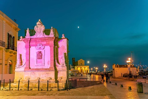 The colourfully illuminated Greek fountain Fontana Greca at dusk, Gallipoli, Apulia, Italy