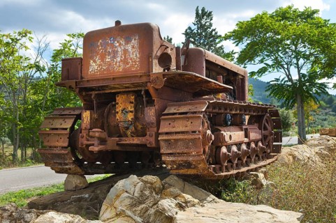 Old, heavily rusted bulldozer for road construction stands abandoned on rocks, industrial relic