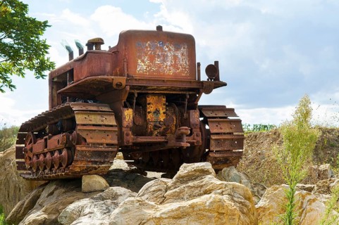 Old, heavily rusted bulldozer for road construction stands abandoned on rocks, industrial relic