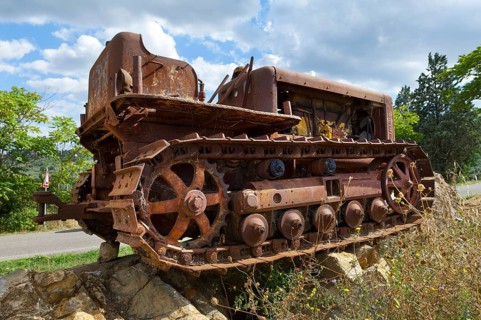 Old, heavily rusted bulldozer for road construction stands abandoned on rocks, industrial relic