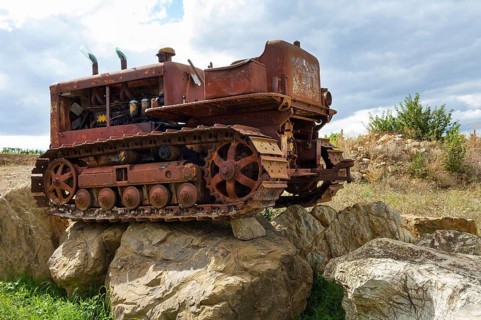 Old, heavily rusted bulldozer for road construction stands abandoned on rocks, industrial relic