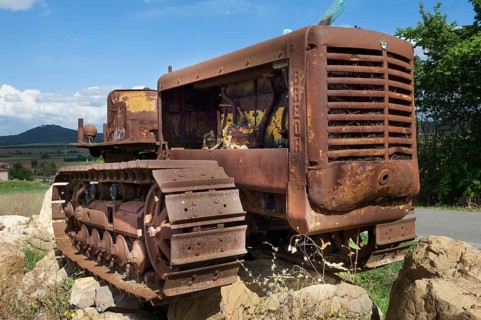 Old, heavily rusted bulldozer for road construction stands abandoned on rocks, industrial relic