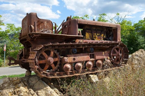 Old, heavily rusted bulldozer for road construction stands abandoned on rocks, industrial relic