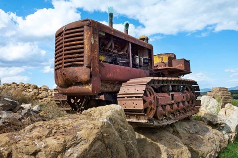 Old, heavily rusted bulldozer for road construction stands abandoned on rocks, industrial relic