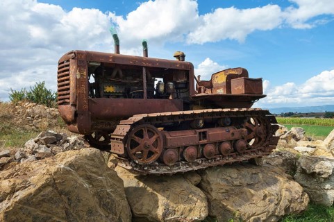 Old, heavily rusted bulldozer for road construction stands abandoned on rocks, industrial relic