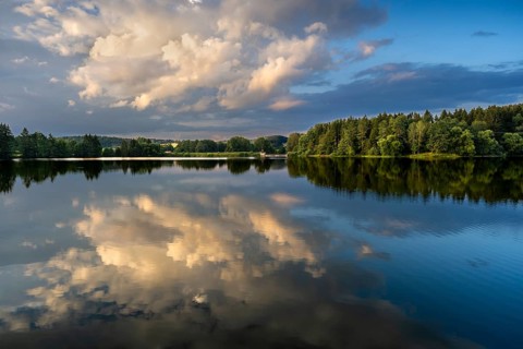 The Postfelden reservoir in the evening at the golden hour. Glowing clouds are reflected in the