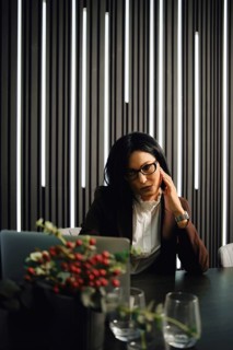 A businesswoman is seated at a desk in a contemporary office, deep in thought, with stylish