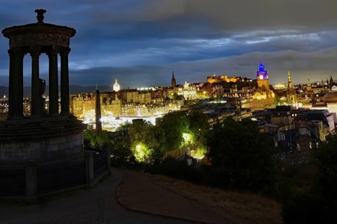 Night view of Edinburgh with illuminated buildings and a historical monument in the foreground, Old