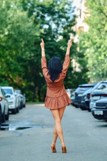 Rear view of a woman walks down a tree-lined street, wearing a fashionable brown outfit and high