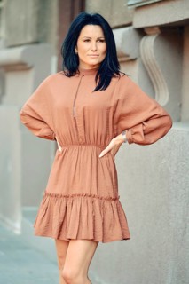 A woman stands with her arms on waist on a city sidewalk, wearing a chic, loose-fitting dress. Her
