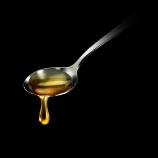 Honey drips from a spoon in front of a black background