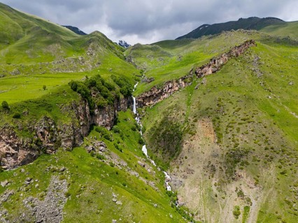 Waterfall cascading down the rocky mountain face, surrounded by green landscape, aerial view, Toti