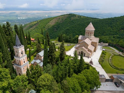 Historic monastery on a green hill surrounded by trees and towers, Bodbe Monastery, Sighnaghi,