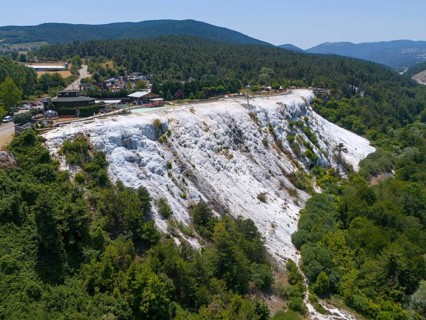 A limestone hillside overlooked by a wooded area under a blue sky, aerial view, Akkaya Travertines,