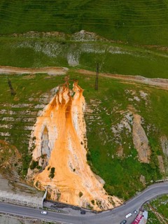 Aerial view of a hill with striking orange rock formation between roads and green landscape, aerial