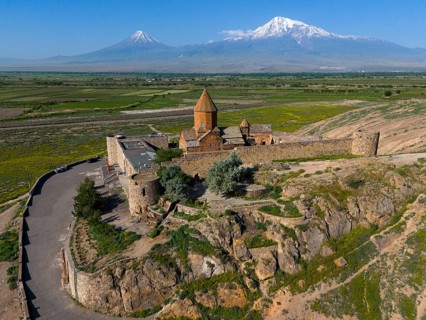 Historic church in a wide landscape in front of impressive mountain peaks under a clear sky, aerial