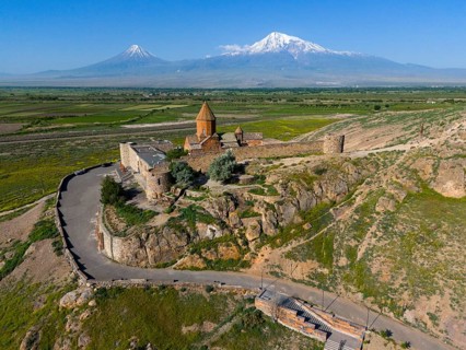 Historical church in front of majestic mountains, embedded in a green landscape with a wide sky,